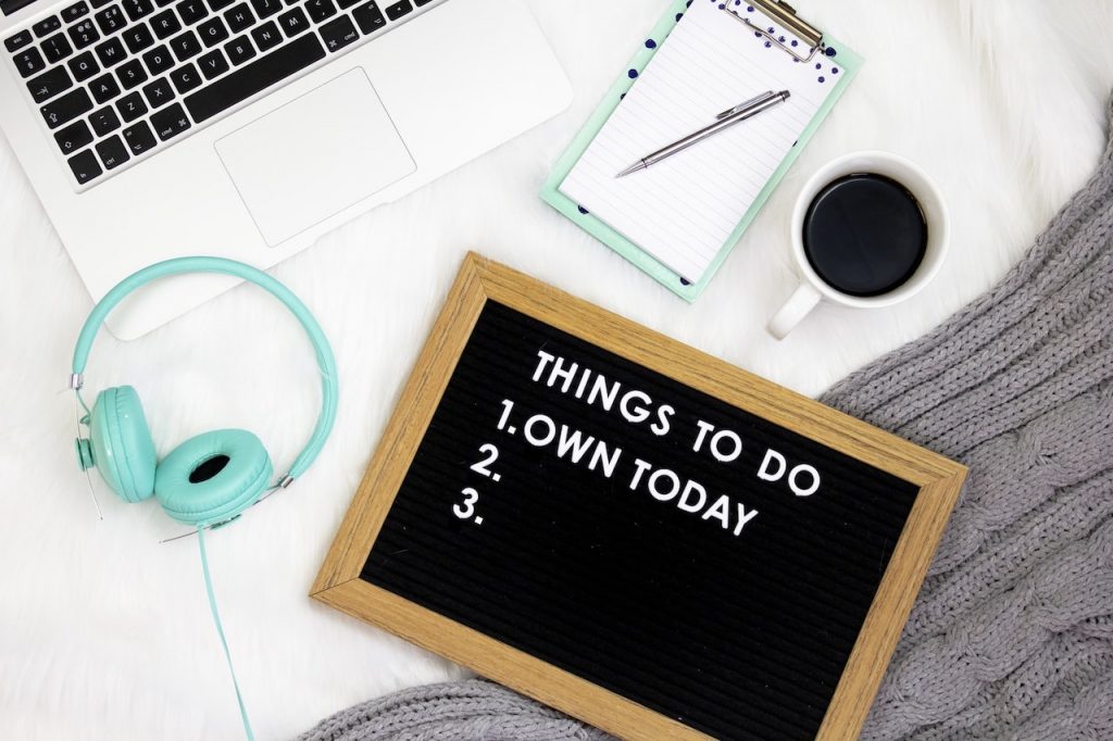 teal headphones, coffee a laptop and a sign that says "Things to do: Own today"