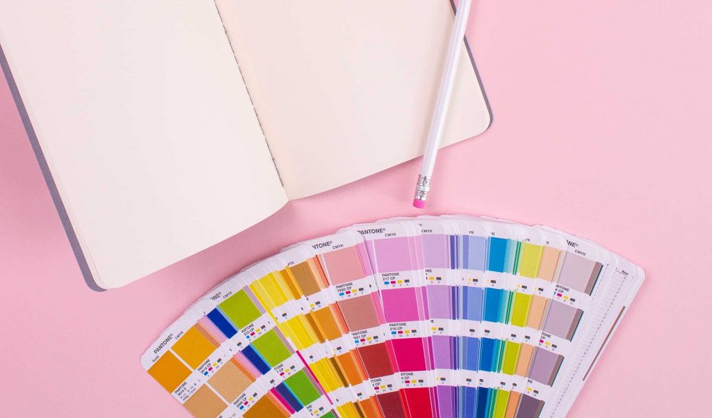 a journal and a pencil are on a pink background with pantone color chips